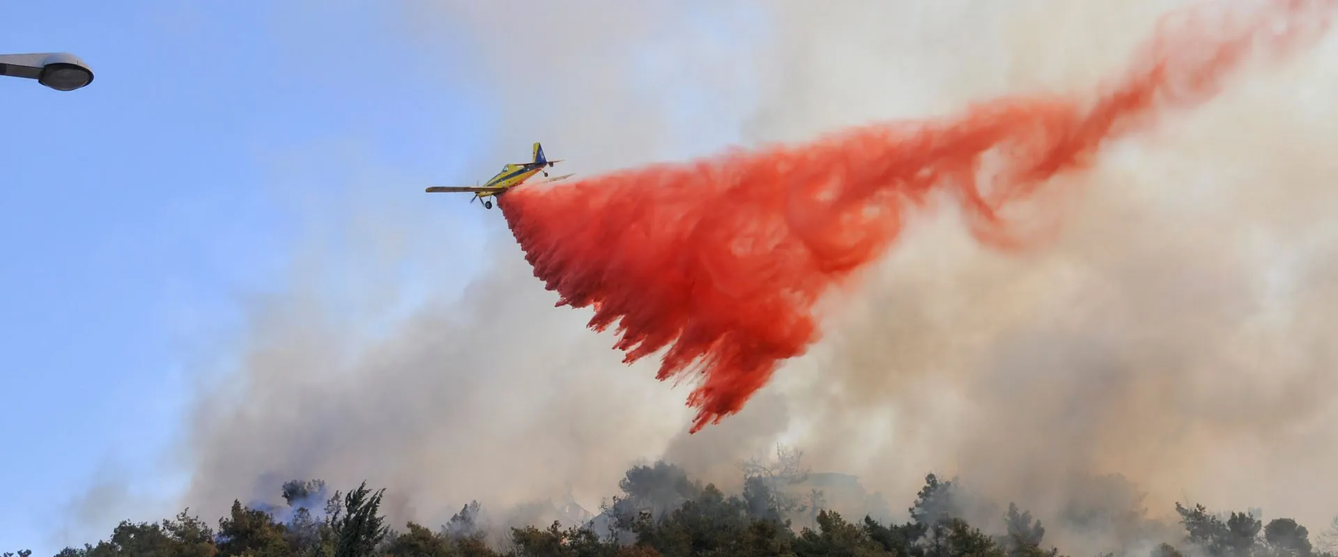 Firefighting aircraft dropping red fire retardant over a forest